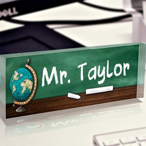 May include: A green chalkboard with the words "Mr. Taylor" written in white chalk. A globe with a blue and green map is on the left side of the chalkboard. There are two pieces of white chalk on the bottom of the chalkboard.