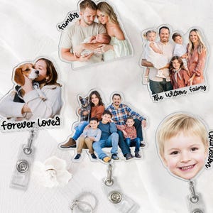 May include: A collection of personalized photo badge reels. Each reel features a family photo, with text overlays such as "Family," "Forever Loved," and names. The reels have a clear plastic body with a retractable cord and a metal clip.
