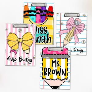May include: Four decorative clipboards with teacher-themed designs. One features crayons, another a yellow bow and pencil, a third a pencil with a pink bow, and the last a yellow pencil with the text "Ms. BROWN". Each has a silver clip.