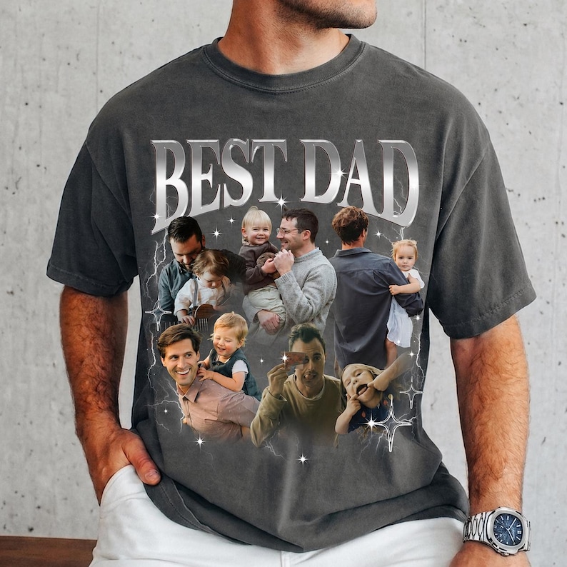 May include: Dark gray t-shirt with the text "BEST DAD" in a silver, metallic font. The shirt features a collage of photos of a father with his children. The photos are surrounded by lightning bolt and star graphics.