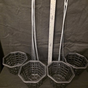 May include: Four black, octagonal hanging baskets with wire hangers. A metal ruler is placed next to the baskets. The baskets are made of a plastic material and have a grid-like design.