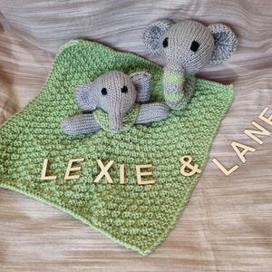 May include: A light green knitted baby blanket with two grey elephant toys. The blanket has the names "LEXIE & LANEY" spelt out in wooden letters. The elephants have black eyes and green accents.