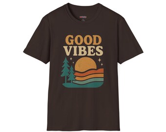 May include: Brown t-shirt with the words "GOOD VIBES" in a retro font. The graphic features a sun, trees, and layered stripes in orange, teal, and brown. A casual, short-sleeved tee.