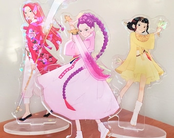 May include: Three anime-style acrylic figures. One figure wears a red floral kimono and holds a staff. Another figure is in a pink dress and holds a sword. The third figure is in a yellow dress and holds a leaf.