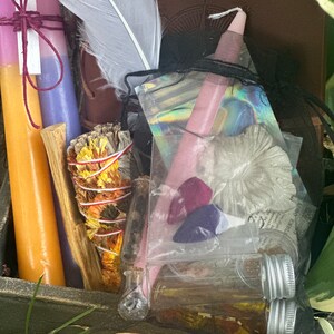 May include: A wooden box filled with various items for a spiritual ritual, including candles, sage, crystals, and a feather. The box is decorated with a copper coin.