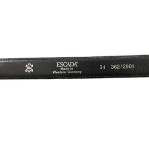 Op de afbeelding: Zwarte leren riem met een zilveren gesp en de tekst "ESCADA Made in Western Germany 34 362/2901" gedrukt op de achterkant.