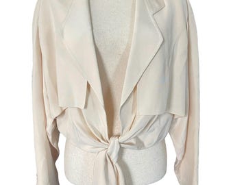 Puede incluir: Una chaqueta de color crema de manga larga, con lazada delantera, cuello y corte ligeramente holgado.