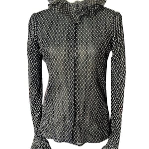 May include: A black sheer blouse with a gold geometric pattern. The blouse has a ruffled collar and ruffled cuffs.