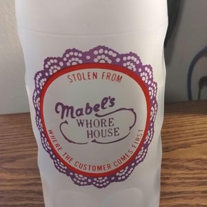 May include: White frosted glass mug with a purple and red circular design that says "Stolen from Mabel's Whore House Where the Customer Comes First."