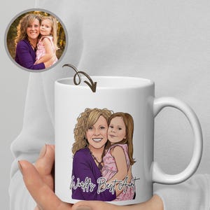 Può includere: Tazza in ceramica bianca con un'illustrazione a cartoni animati di una donna e una bambina, con la scritta "World's Best Aunt". La tazza ha un manico curvo e una foto degli stessi soggetti in un cerchio.