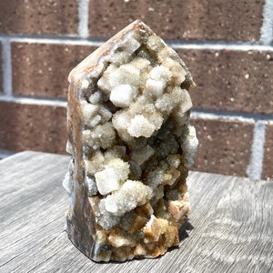 May include: A brown and white crystal cluster with a pointed top. The crystal is a natural formation with a rough texture.
