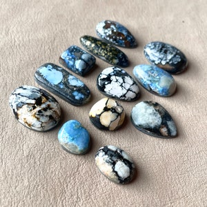 May include: A collection of 11 polished cabochons in various sizes and shapes, featuring a mix of white, black, and blue colours. The stones have a unique, marbled pattern and are ideal for jewellery making.