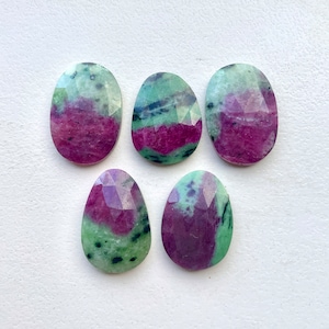 May include: Five oval-shaped green and pink gemstones with a faceted cut. The stones have a mottled appearance with green, pink, and black swirls.