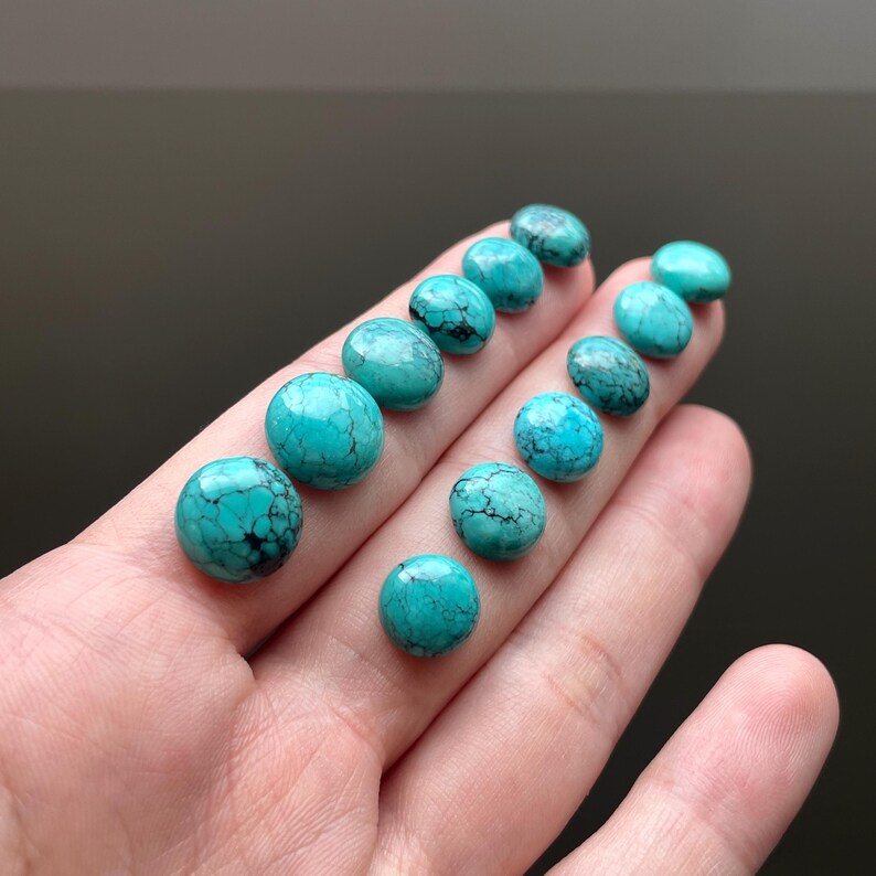 May include: A collection of turquoise cabochons, each with a unique pattern of veins and a smooth, polished surface. The cabochons are a vibrant blue-green color and are arranged in a row on a hand.