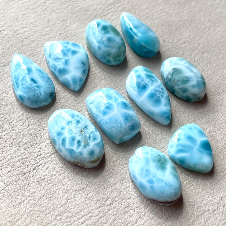 May include: Ten smooth, oval-shaped, light blue and white gemstone cabochons. The stones have a swirling, marbled pattern.