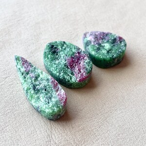 May include: Three teardrop-shaped green and pink gemstones with a mottled pattern.