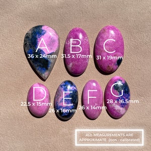 May include: Six pink and blue cabochon stones with black markings. The stones are labeled A through G and have measurements in millimeters. The text "ALL MEASUREMENTS ARE APPROXIMATE (non - calibrated)" is at the bottom of the image.