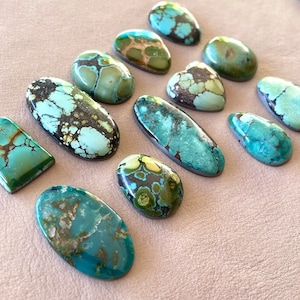 Op de afbeelding: Een verzameling van 12 turquoise cabochons in verschillende vormen en maten. De stenen zijn een mix van blauwe, groene en bruine kleuren met een marmerpatroon.