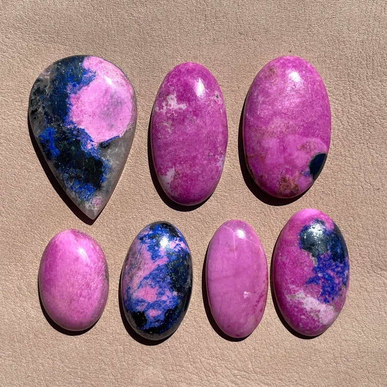 May include: Seven cabochon gemstones, six oval and one teardrop shaped, with pink and blue marbling. The stones are polished and have a smooth, glossy finish.