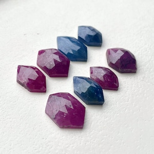 May include: A collection of faceted gemstones in shades of pink and blue. The stones are arranged in a row, with the pink stones on the left and the blue stones on the right.
