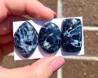 Può includere: Tre cabochon di occhio di tigre blu, uno ovale, uno rettangolare e uno a forma di lacrima. Le pietre hanno un effetto scintillante e iridescente.