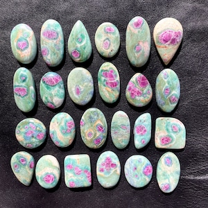 May include: Twenty-two green and pink ruby zoisite cabochons, each with a unique pattern of pink and green. The cabochons are smooth and polished, and they are arranged in a grid pattern on a black surface.