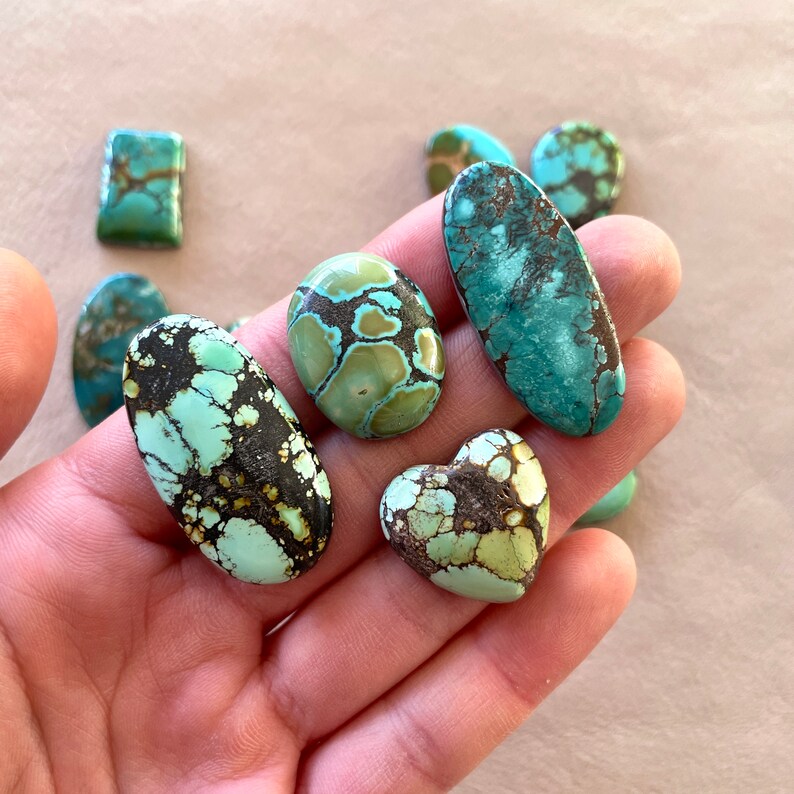 Op de afbeelding: Assortiment van turquoise cabochons in verschillende vormen en maten, waaronder ovaal, hartvormig en vierkant. De stenen hebben een mix van groene, blauwe en bruine kleuren met een gevlekt patroon.