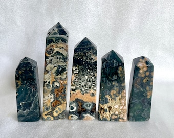 May include: Five green, black, and white jasper point crystals. The crystals are arranged in a row from smallest to largest. The crystals are polished and have a smooth, shiny surface.