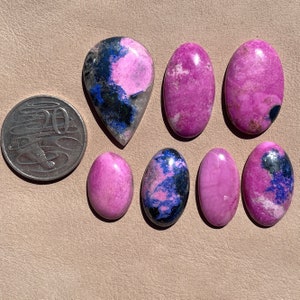 May include: A collection of eight pink and blue cabochon gemstones. The stones are oval and teardrop shaped and have a variety of patterns and textures.