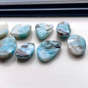 May include: A collection of eight blue, white, and brown gemstone cabochons. The cabochons are teardrop shaped and have a smooth, polished finish.