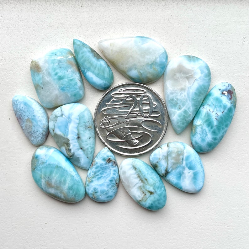 May include: A collection of 11 blue and white gemstone cabochons, some with a pear shape and others with a more rounded shape. The stones are arranged around a 20 cent Australian coin for scale.