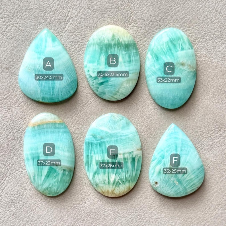May include: Six polished amazonite gemstones in various shapes, including oval and teardrop. Each stone is a mix of light blue and white with visible patterns. Measurements are included for each stone, ranging from 30x24.5mm to 37x26mm.