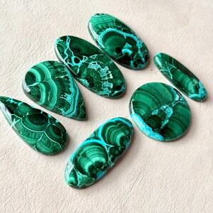 Pu&ograve; includere: Una collezione di sei pietre preziose di malachite lucidata in varie forme, tra cui goccia, ovale e circolare. Ogni pietra mostra tonalit&agrave; verde intenso con intricati motivi a bande vorticose e una finitura superficiale liscia.