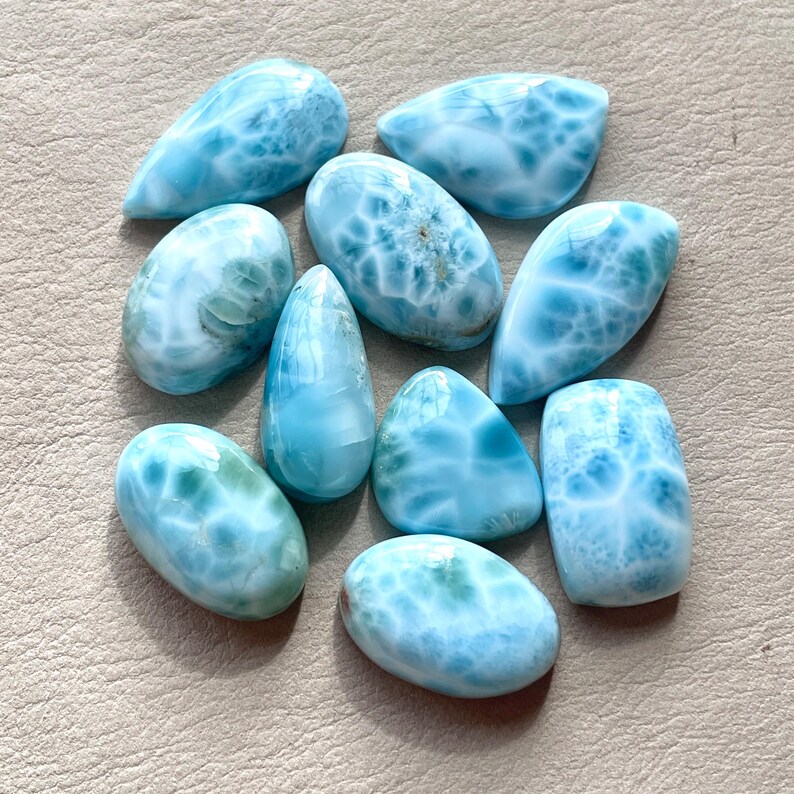 May include: A collection of ten blue and white gemstone cabochons. The cabochons are all different shapes and sizes, but they all have a similar swirling pattern.