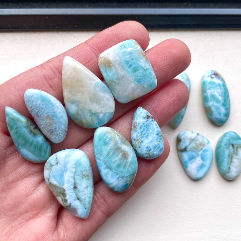 May include: A collection of ten blue and white cabochon gemstones with a swirling pattern. The stones are various shapes and sizes, including teardrop, oval, and square.