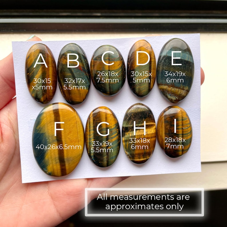 May include: Eight oval-shaped tiger's eye cabochons in various sizes, labeled A through I. Each stone is a different size and has a unique pattern of brown, gold, and blue colors. The stones are arranged in two rows on a white background. All measurements are approximates only.