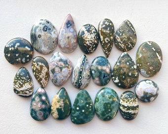 May include: A collection of 17 green, white, and brown ocean jasper cabochons. The cabochons are all teardrop shaped and have a variety of patterns.
