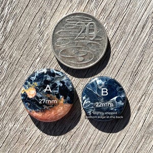 May include: Two round, blue, black, and orange tiger's eye cabochons. The larger cabochon is 27 mm in diameter and the smaller cabochon is 22 mm in diameter. The smaller cabochon has a slightly chipped bottom edge.