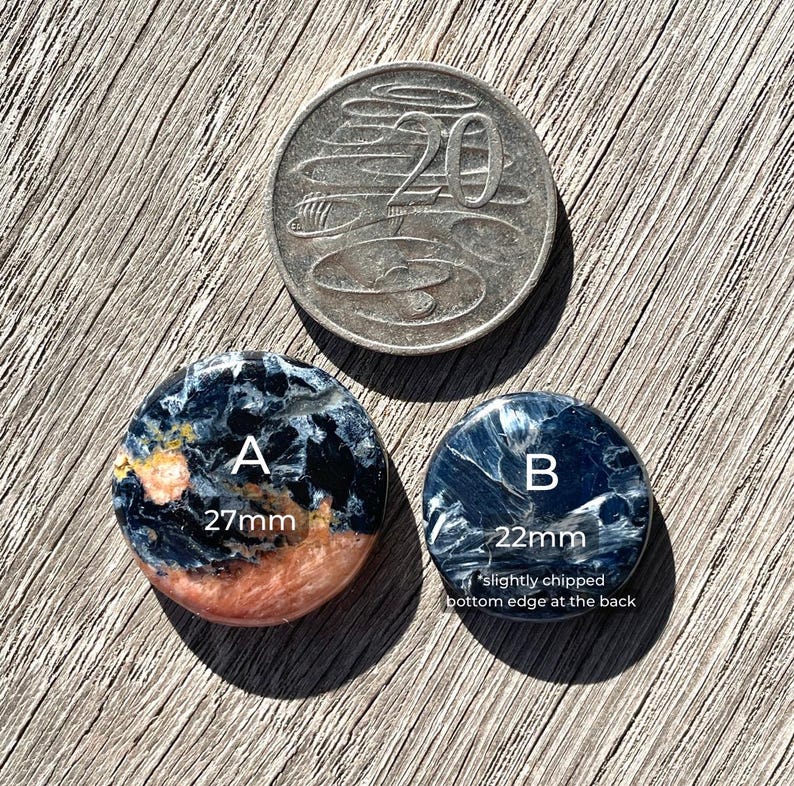 May include: Two round, blue, black, and orange tiger's eye cabochons. The larger cabochon is 27 mm in diameter and the smaller cabochon is 22 mm in diameter. The smaller cabochon has a slightly chipped bottom edge.