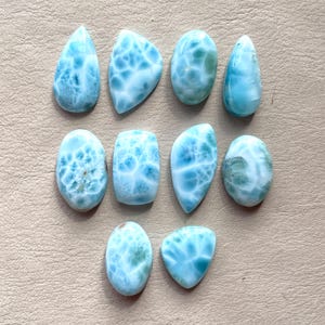 May include: A collection of ten blue and white gemstone cabochons. The cabochons are various shapes and sizes, with a swirling, marbled pattern.