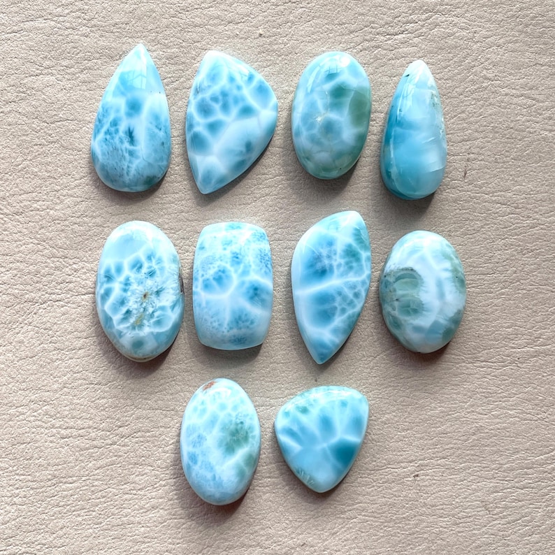 May include: A collection of ten blue and white gemstone cabochons. The cabochons are various shapes and sizes, with a swirling, marbled pattern.
