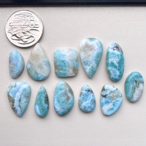 May include: A collection of twelve blue and white gemstone cabochons, some with a teardrop shape, others oval, and one square. The stones have a marbled pattern and are arranged on a white surface.