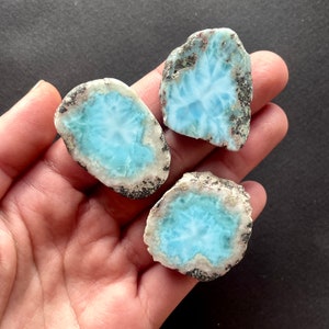 May include: Three blue and white ocean jasper stones with a rough, natural edge. The stones are translucent and have a swirling pattern.