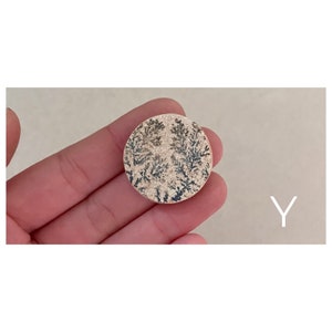 Puede incluir: Una piedra redonda de color beige con un patr&oacute;n dendr&iacute;tico gris oscuro. La piedra es aproximadamente del tama&ntilde;o de una moneda de 20 c&eacute;ntimos de euro.