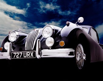 May include: A black classic Jaguar XK150 roadster with chrome accents and a license plate that reads "727 URX". The car is parked against a blue sky with white clouds.
