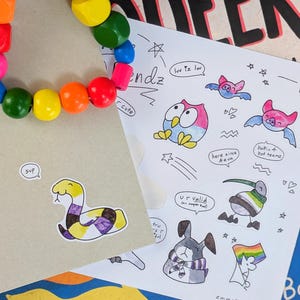 Pode incluir: Uma folha de autocolantes com ilustrações coloridas desenhadas à mão de animais, incluindo uma cobra, uma coruja, morcegos e um coelho, com balões de fala contendo texto como 'sup', 'luv iz lw', 'here since Aeva' e 'U r valid'.