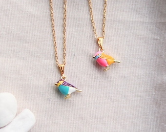 Può includere: Due collane color oro con ciondoli a forma di uccello. Un ciondolo è blu, turchese, bianco e viola. L'altro ciondolo è rosa, arancione e blu. Gli uccelli hanno zampe color oro e sono su catene d'oro.