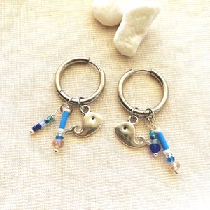 Könnte beinhalten: Ein Paar silberne Creolen mit Wal-Anhängern. Jeder Ohrring hat einen kleinen silbernen Wal-Anhänger und eine Ansammlung blauer, klarer und rosa Perlen. Die Ohrringe werden auf einer hellen Oberfläche präsentiert.