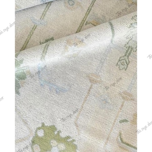 May include: Close-up of a beige rug with a floral pattern. The rug features green, blue, and tan floral and botanical designs. The rug is folded over, showing the texture and detail of the weave.