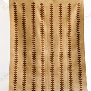 Op de afbeelding: Beige tapijt met verticale rijen bruine driehoekpatronen. Het tapijt is rechthoekig en lijkt gemaakt van een geweven materiaal. Het tapijt wordt door onzichtbare handen omhooggehouden.